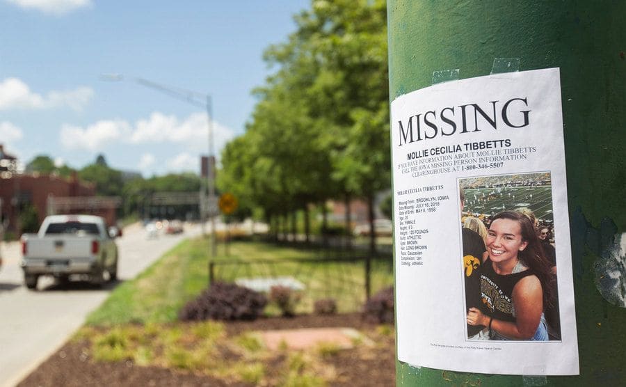 A missing person flyer looking for a young girl hung up on a lamppost. 