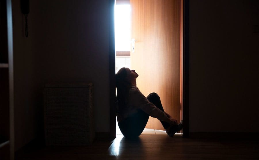 A teenager is sitting in a dark indoor doorway.