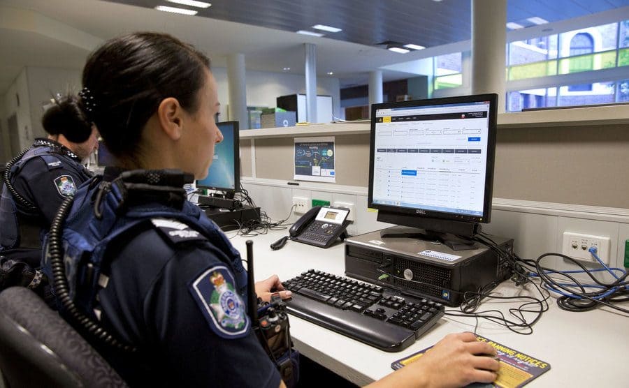 A police officer is sitting at a computer keeping track of the tips received. 