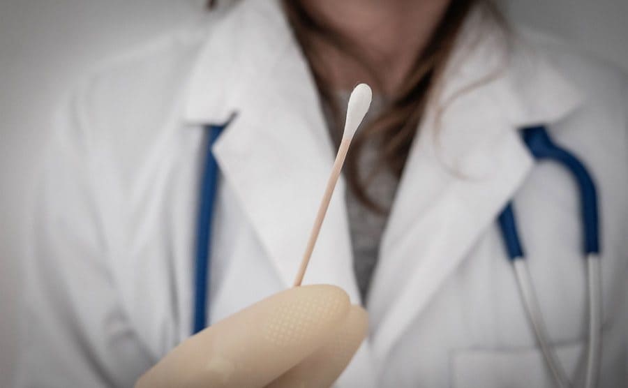 A close-up of a female doctor hand holding a cotton swab.