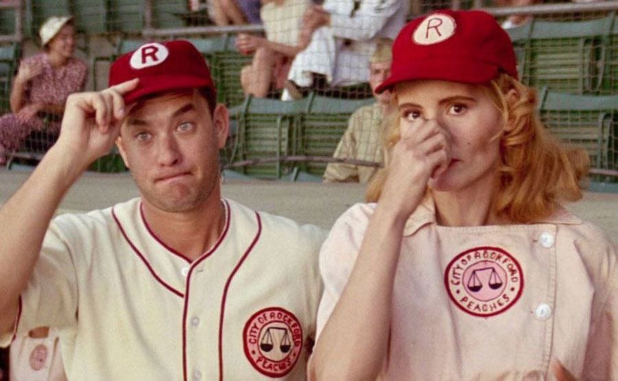 Tom Hanks and Geena David are making hand signals to the players from the dugout during a game. 