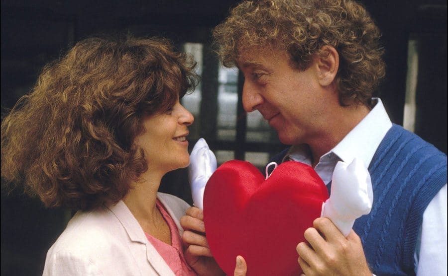 Gene and Gilda holding up a plush heart-shaped doll between them. 