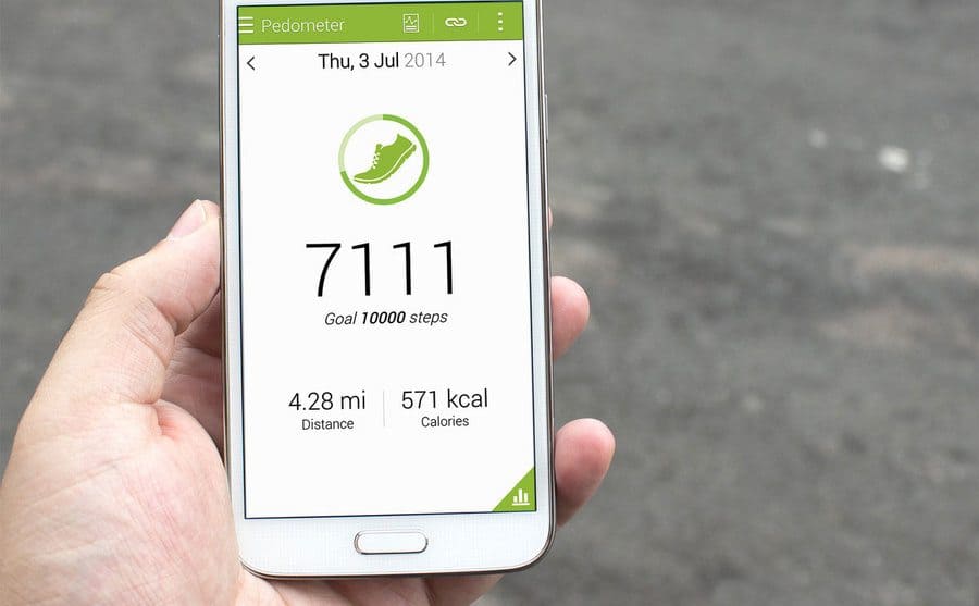 A hand holding up a smartphone open on a step count app. 