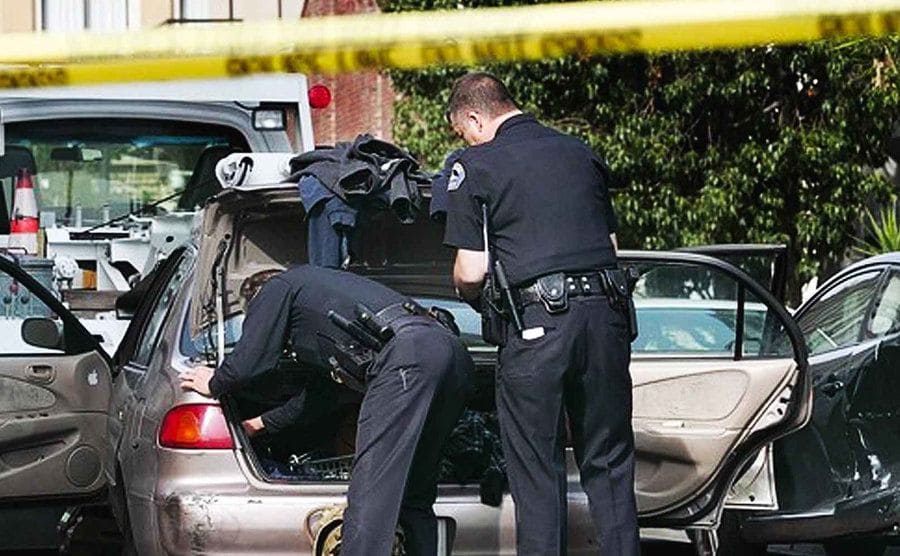 Two police officers search the trunk of a car. 