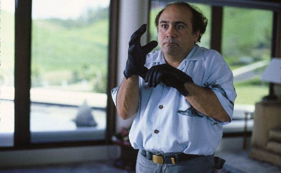 Danny DeVito is putting on gloves in a scene from “Throw Momma from the Train”. 