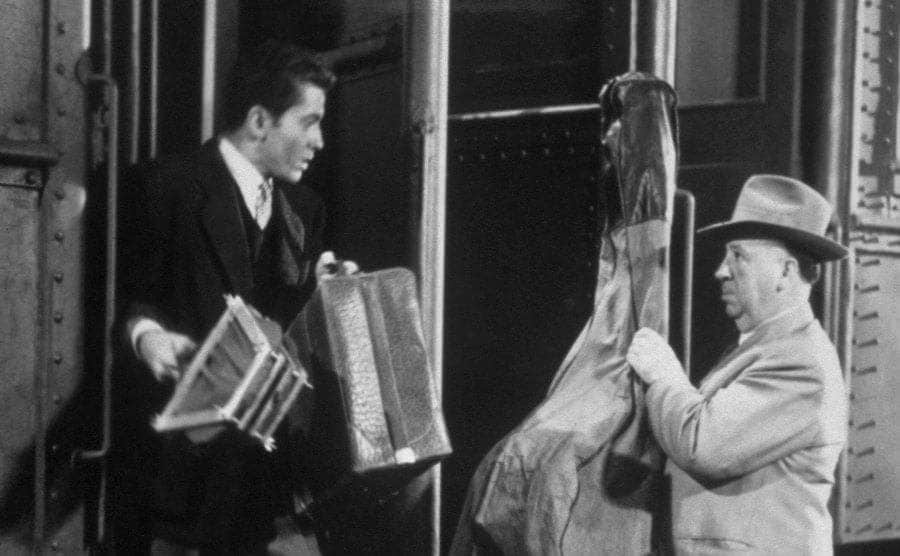 Farley Granger is getting off the train as Alfred Hitchcock gets on with a cello in a still from 'Strangers on a Train'.