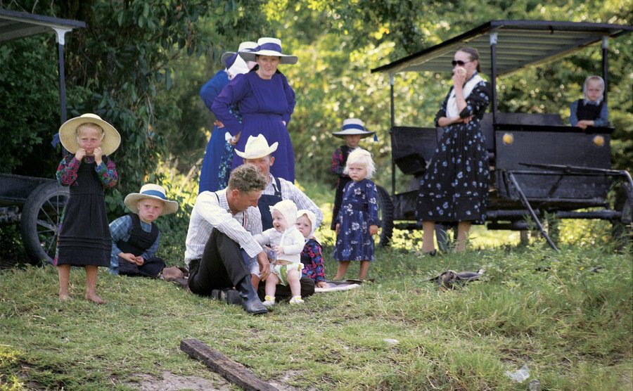 An Amish family sits down for a picnic on the grass. 