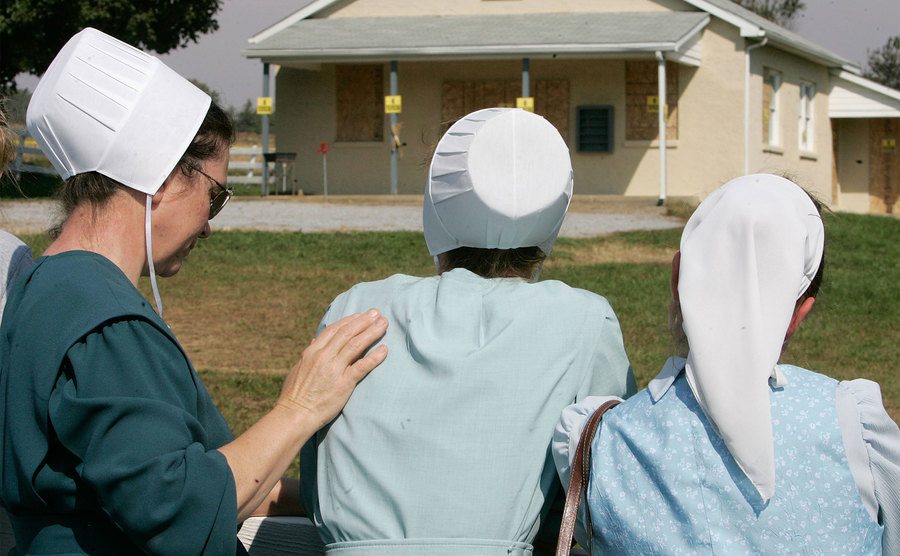 An older Amish woman places her hand on a younger girl's shoulder as a sign of support. 