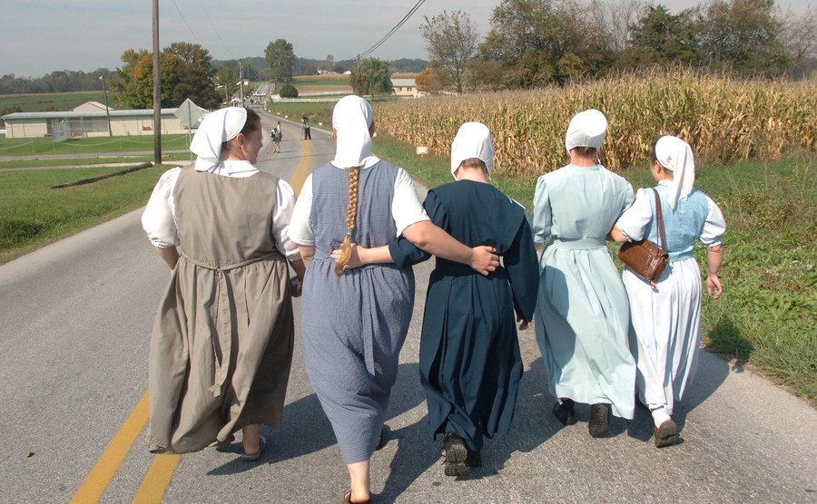 Five Amish women walk hand in hand down the road. 