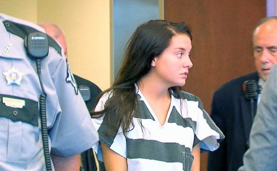 Shayna Hubers looking confused, entering the courtroom surrounded by police officers.