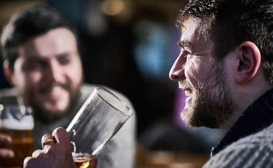 A profile portrait of a man drinking a beer in a pub laughing with his friend.