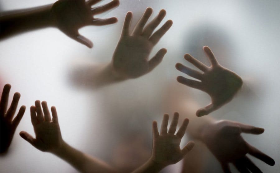 Many hands in silhouette pressed against a frosted glass.