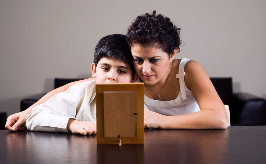 Mother and her son are looking longingly at a picture in a frame. 