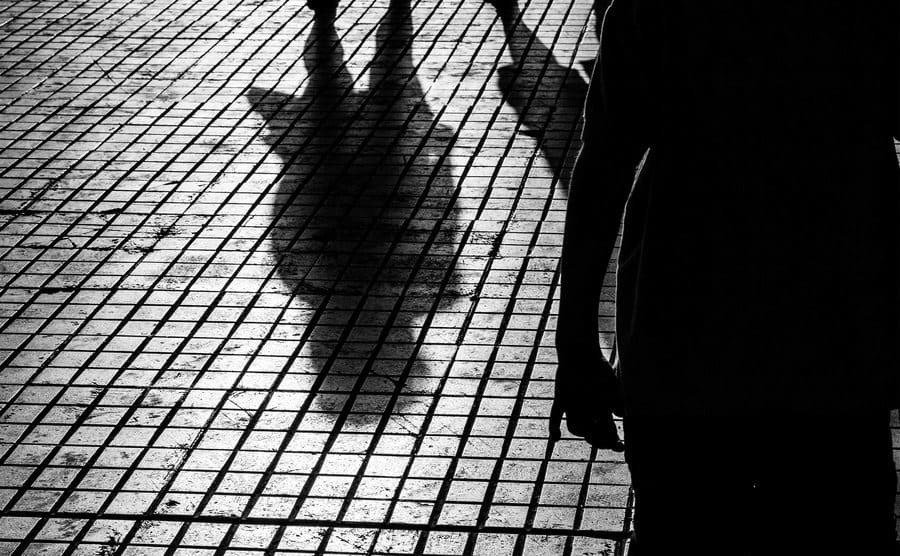 A shadowed figure follows a person down the street. 