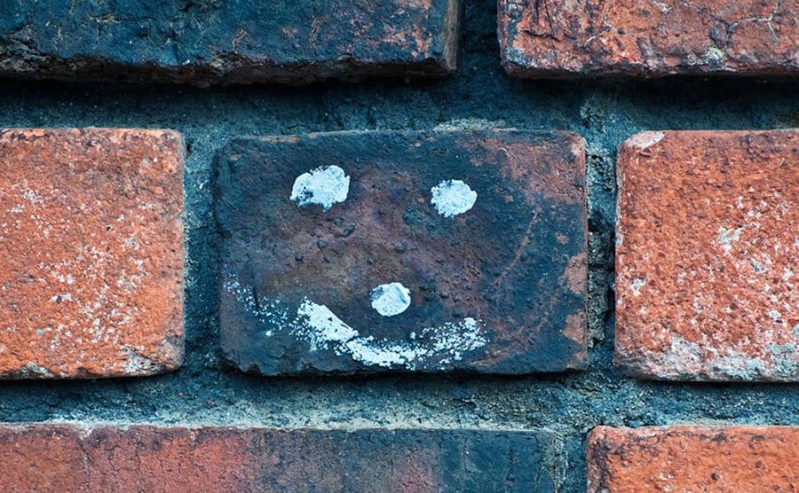 A small smiley face has been graffitied on a brick wall. 