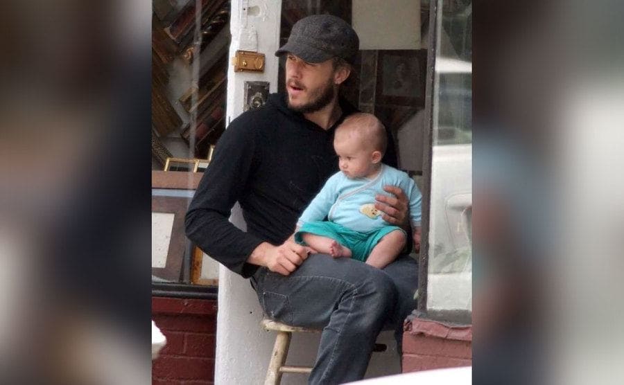 Heath Ledger is holding his daughter on his lap. 