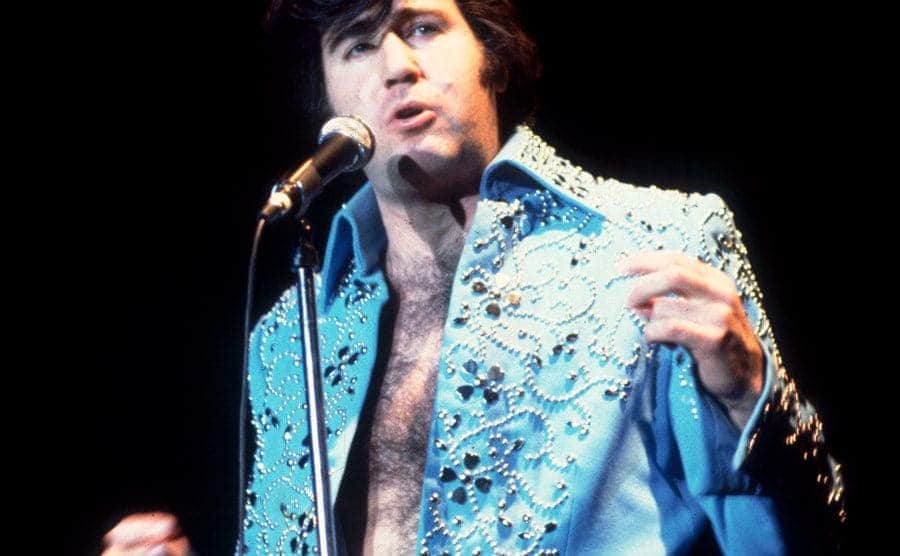 Andy Kaufman is performing on stage as Elvis Presley.