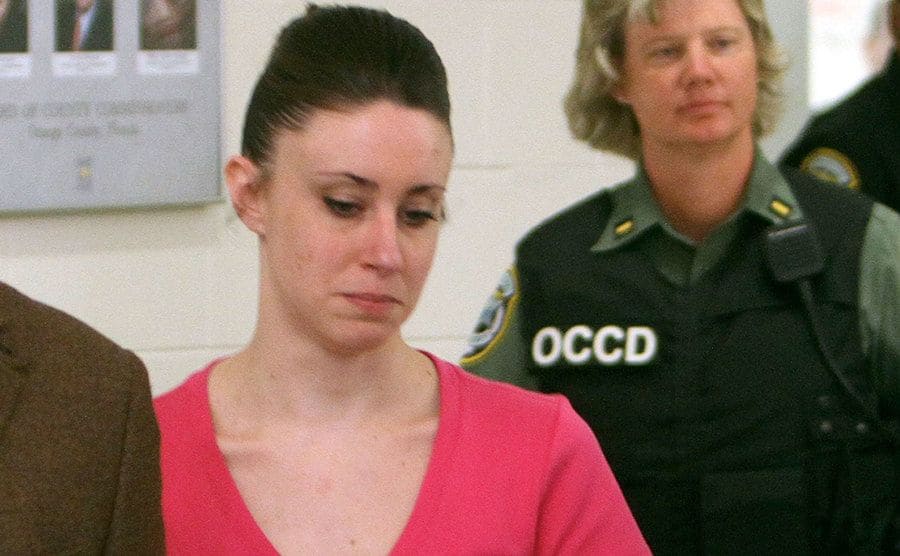 A police officer walks behind Casey Anthony.