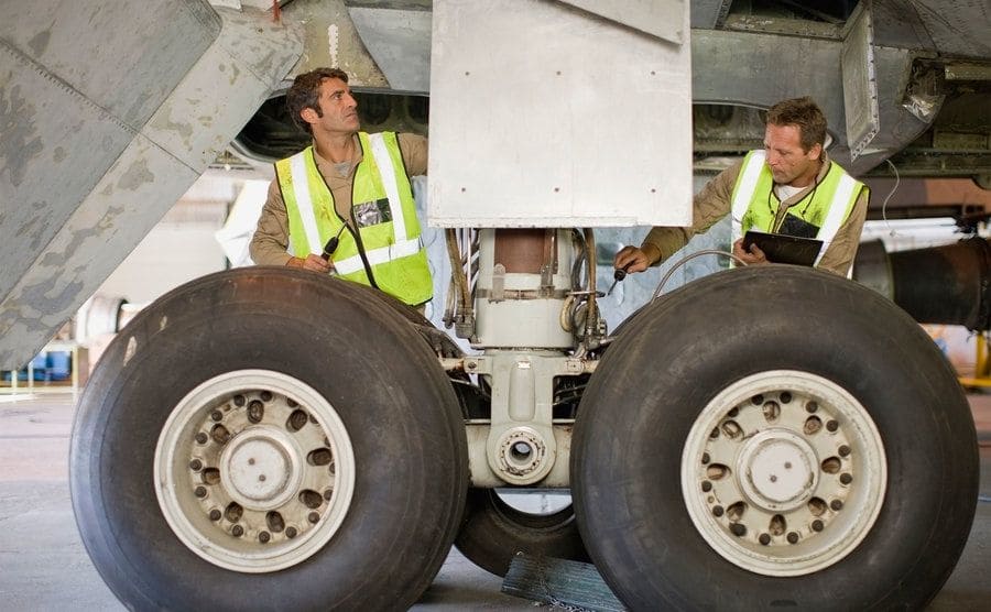 Aircraft workers are checking the landing gear. 