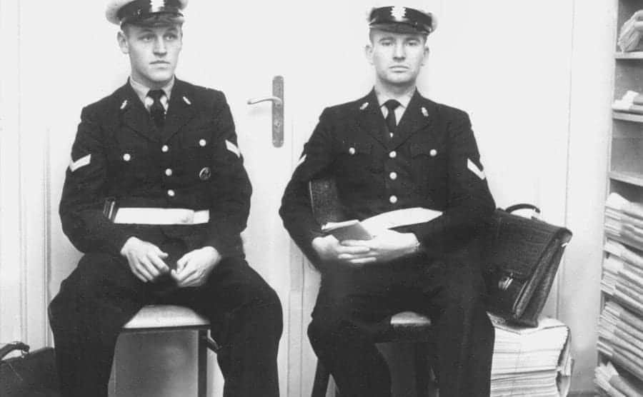 Two police officers frontally facing the camera sitting in silence.