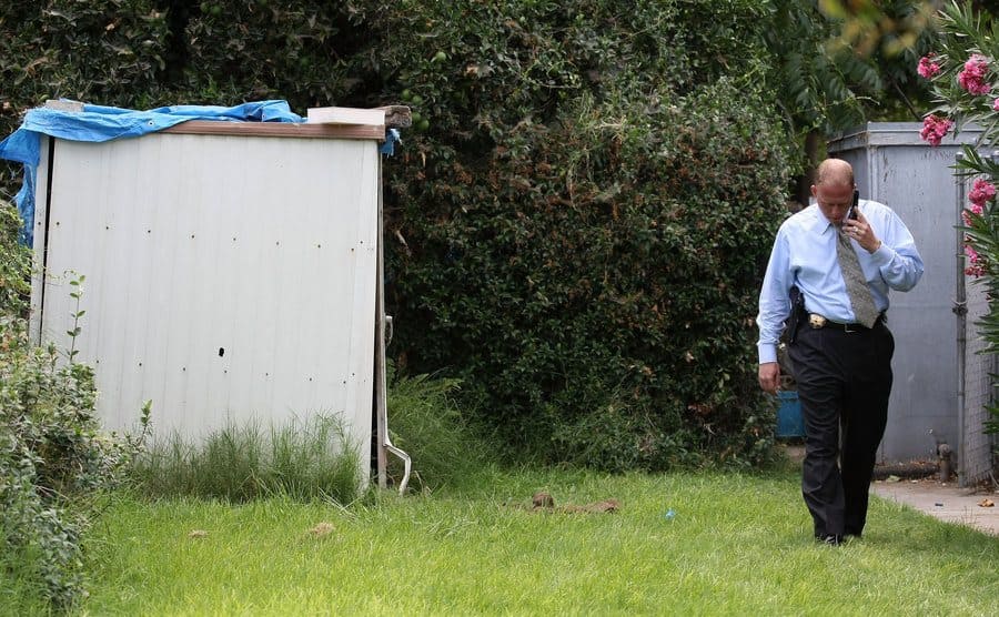 A police officer is walking through the yard past a shed at the home of the kidnapper Phillip Garrido.