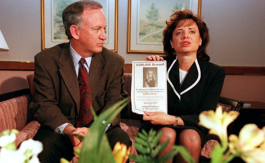 Patsy Ramsey holds up a reward sign for information leading to the arrest of their daughter's murderer as she sits on the couch beside her husband. 