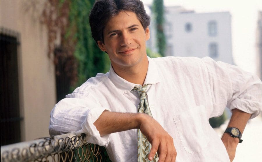 An outdoors TV still of Thomas as Michael Mancini leaning on a fence.