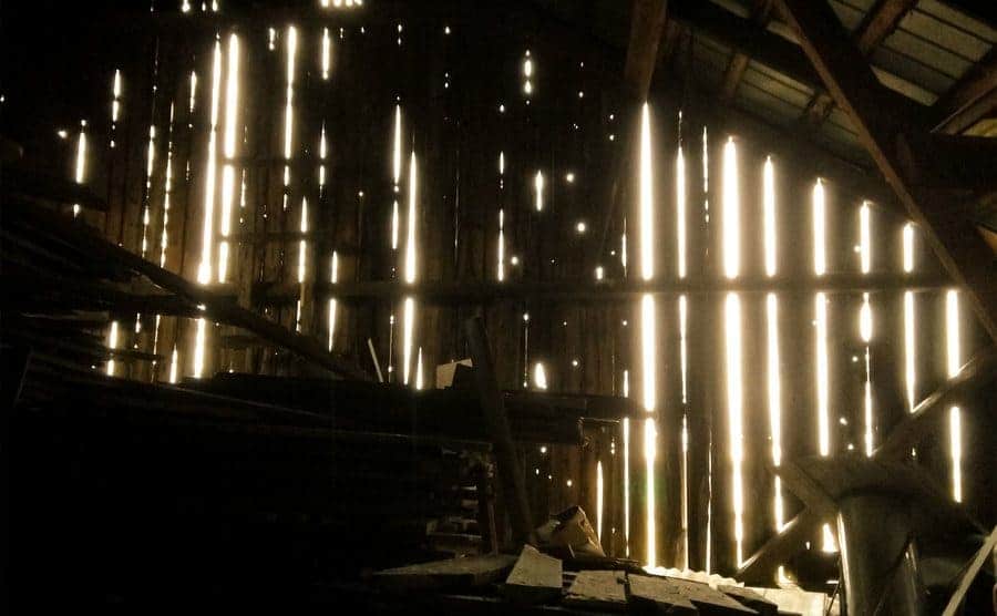 Interior of a barn slightly illuminated by the sun entering through the wooden planks.