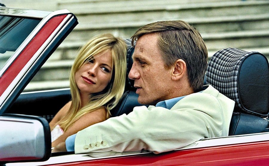Sienna Miller and Daniel Craig are sitting at the front seats of a convertible car.