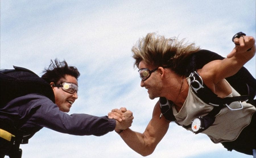 Swayze and Reeves hold hands as they skydive. 