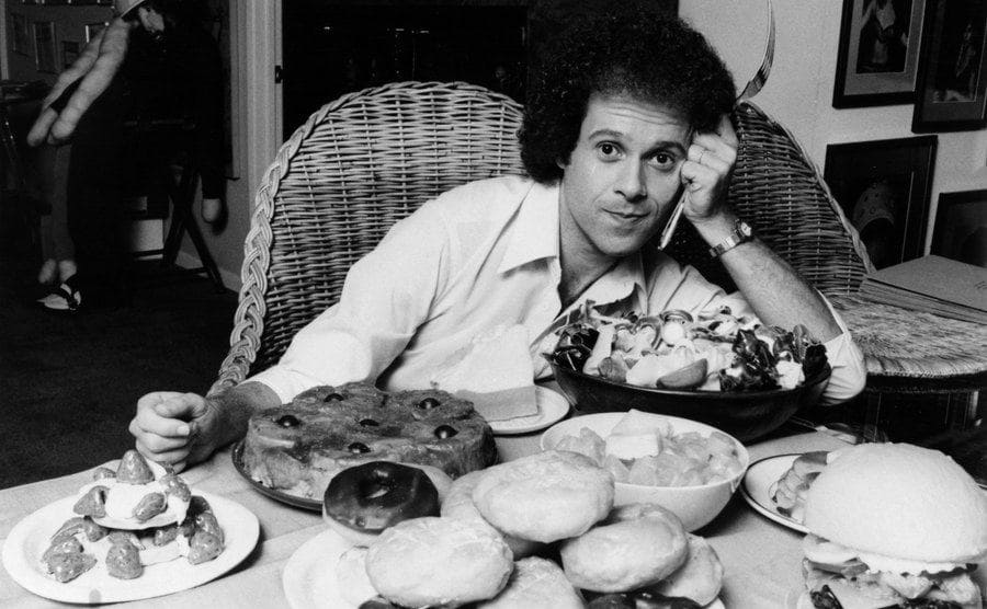 Richard Simmons poses for a portrait session with a table full of food.