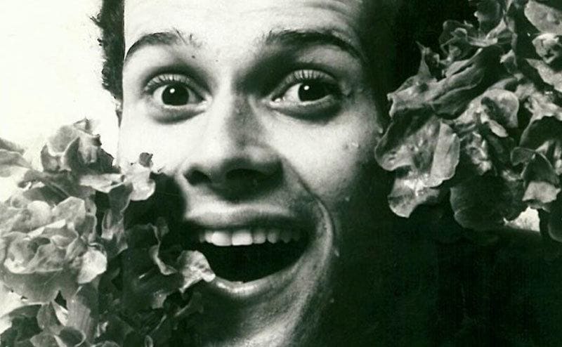A younger Richard Simmons poses in between green vegetable leaves.