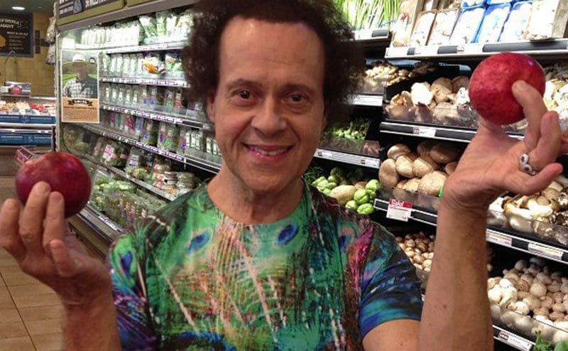 Richard Simmons poses, holding apples at the supermarket.