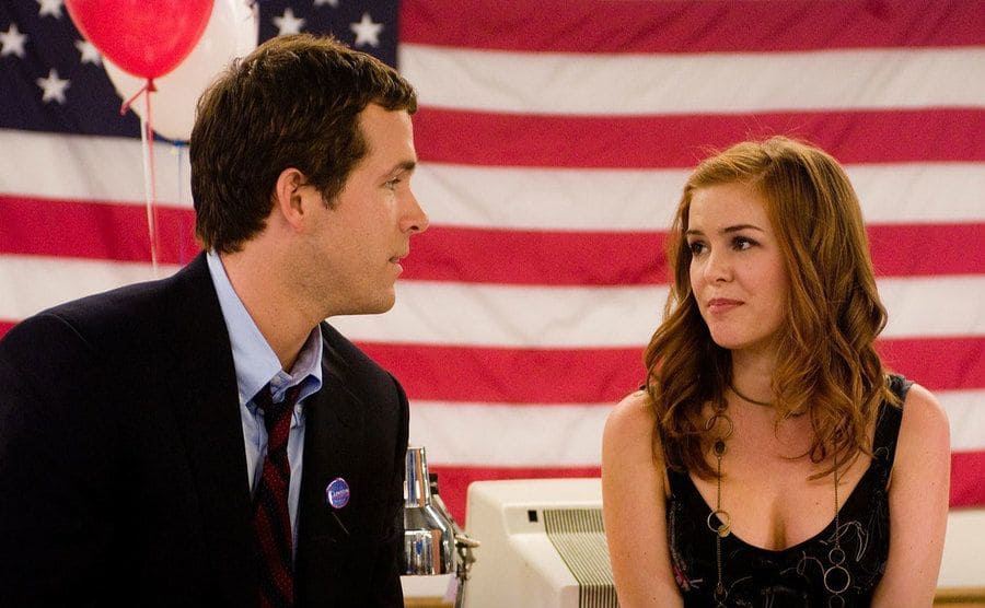 Ryan Reynolds and Isla Fisher are sitting before the U.S. flag in a still from Definitely, Maybe. 
