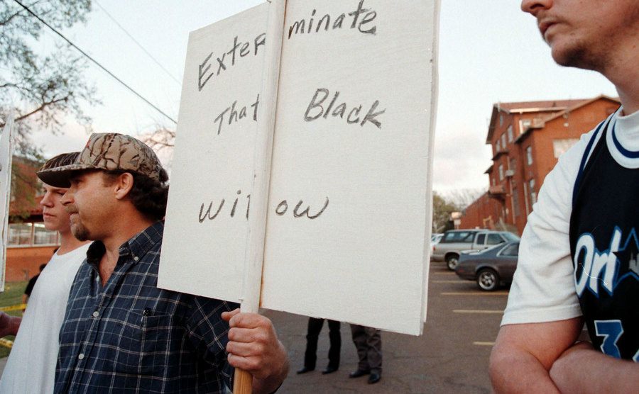 A man holds a sign that reads ‘’Exterminate That Black Widow.’’