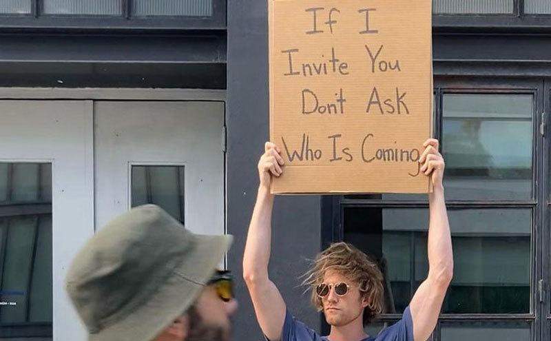 A man is holding a sign that reads ‘’If I Invite You, Don’t Ask who’s Coming.’’