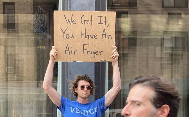 A man is holding a sign that reads ‘’We Get it, You Have an Air Fryer.’’