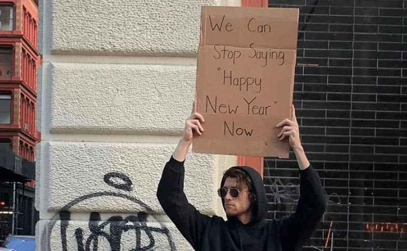 A man is holding a sign that reads, ‘’We Can Stop Saying Happy New Year Now.’’