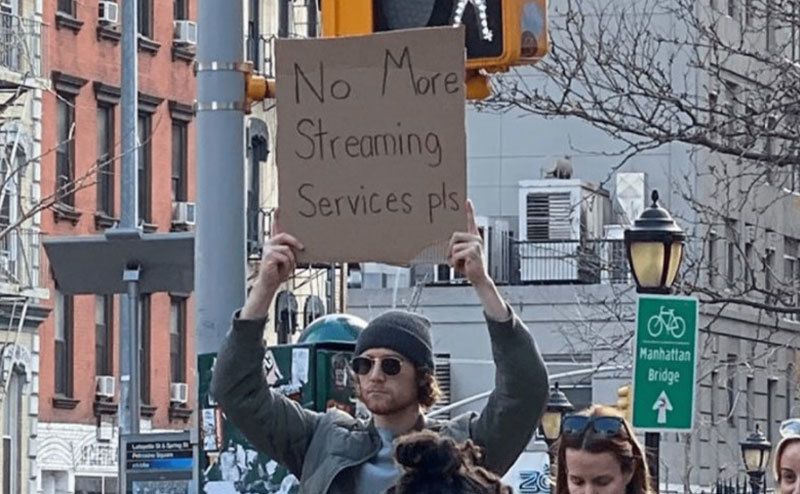 A man is holding a sign that reads ‘’No More Streaming Services Please.’’