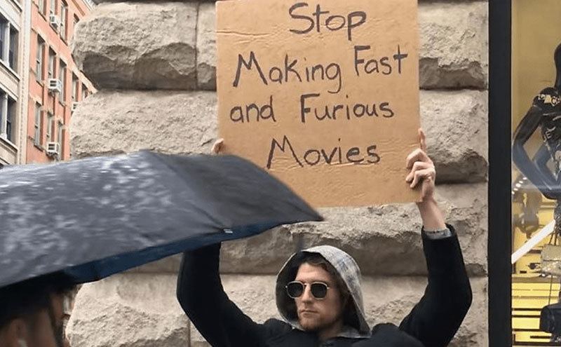 A man is holding a sign that reads ‘’Stop Making Fast and Furious Movies.’’