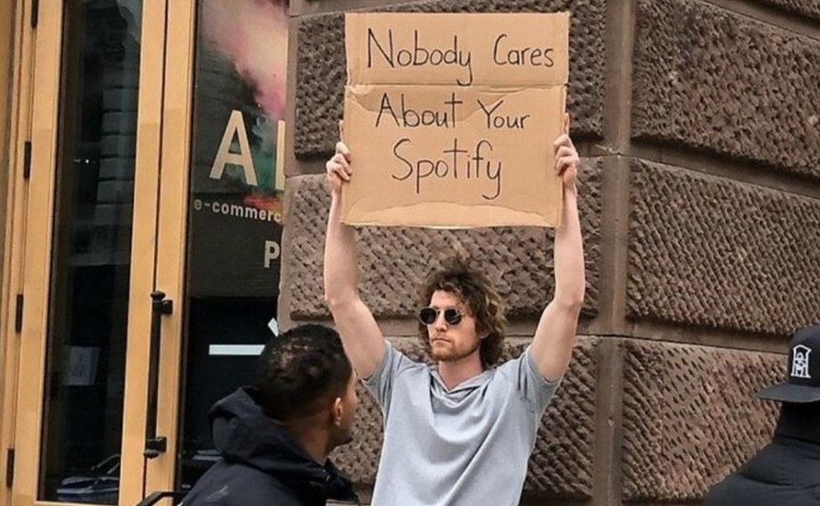 A man is holding a sign that reads ‘’Nobody Cares About Your Spotify.’’