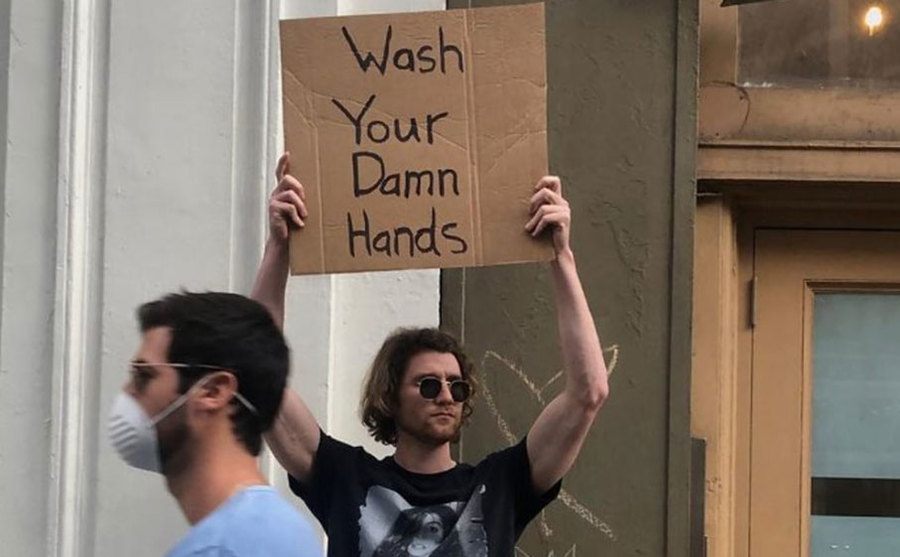 A man is holding a sign that reads ‘’Wash Your Hands.’’