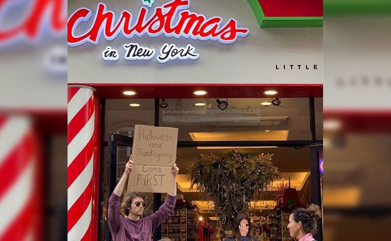A man is holding a sign that reads ‘’Halloween and Thanksgiving Come First.’’