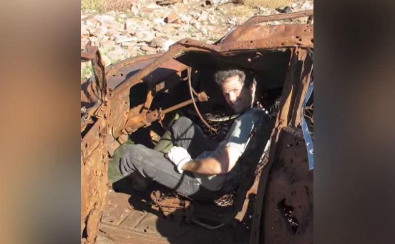 Kenny sits inside an abandoned car in the desert. 
