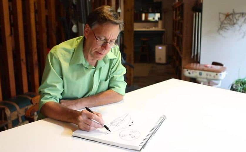 Bob Lazar sits drawing a UFO at his desk. 