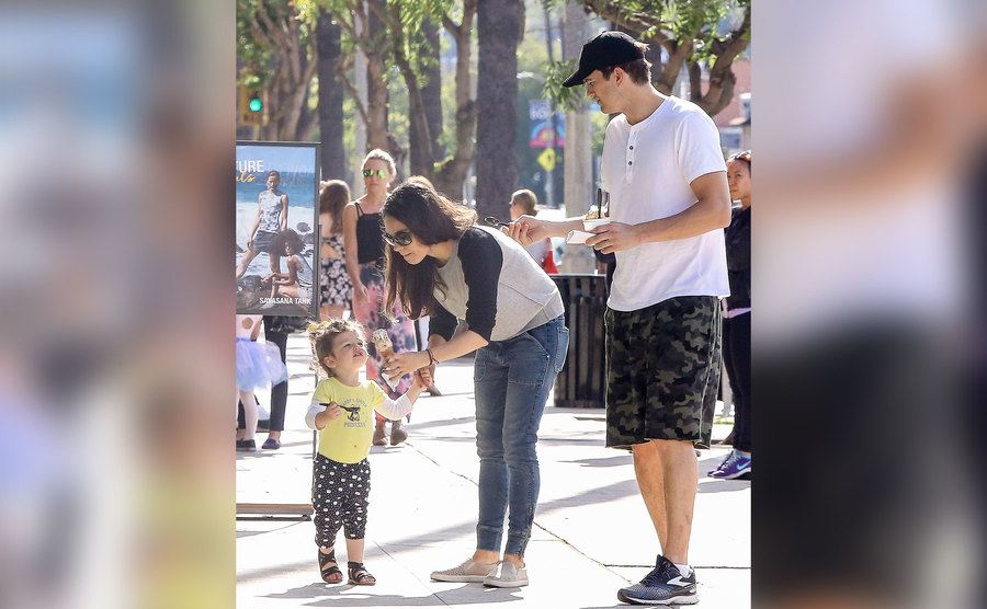 Ashton and Mila offer their daughter Wyatt some ice cream as they walk down the street. 
