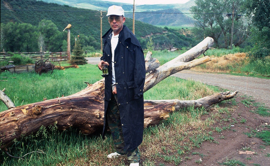 Hunter Thompson is at his ranch, standing next to a fallen tree. 