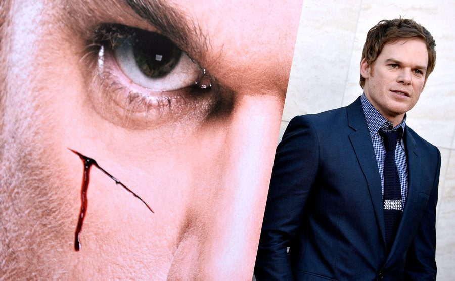 Michael C. Hall stands before a promotional poster of Dexter.