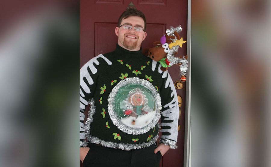 A man is wearing a sweater with a 3D snow globe on it. 