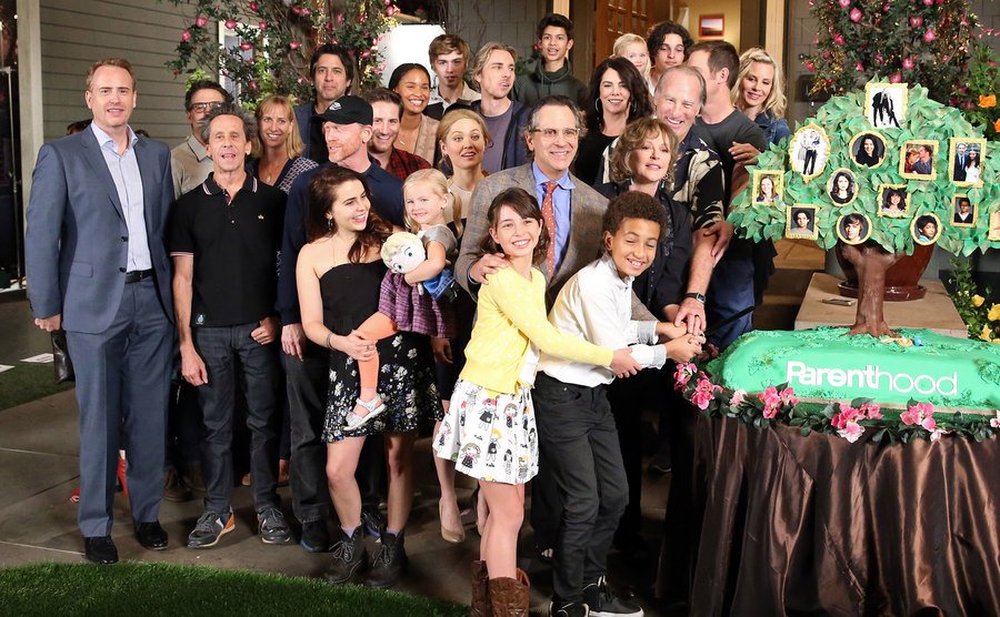 Parenthood cast pose at the 100th episode cake-cutting ceremony.